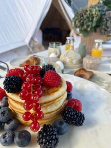 Verse homemade Amerikaanse pannenkoeken met vers fruit op de ontbijttafel met op de achtergrond de glamping tent van onze B&B in Vorden.
