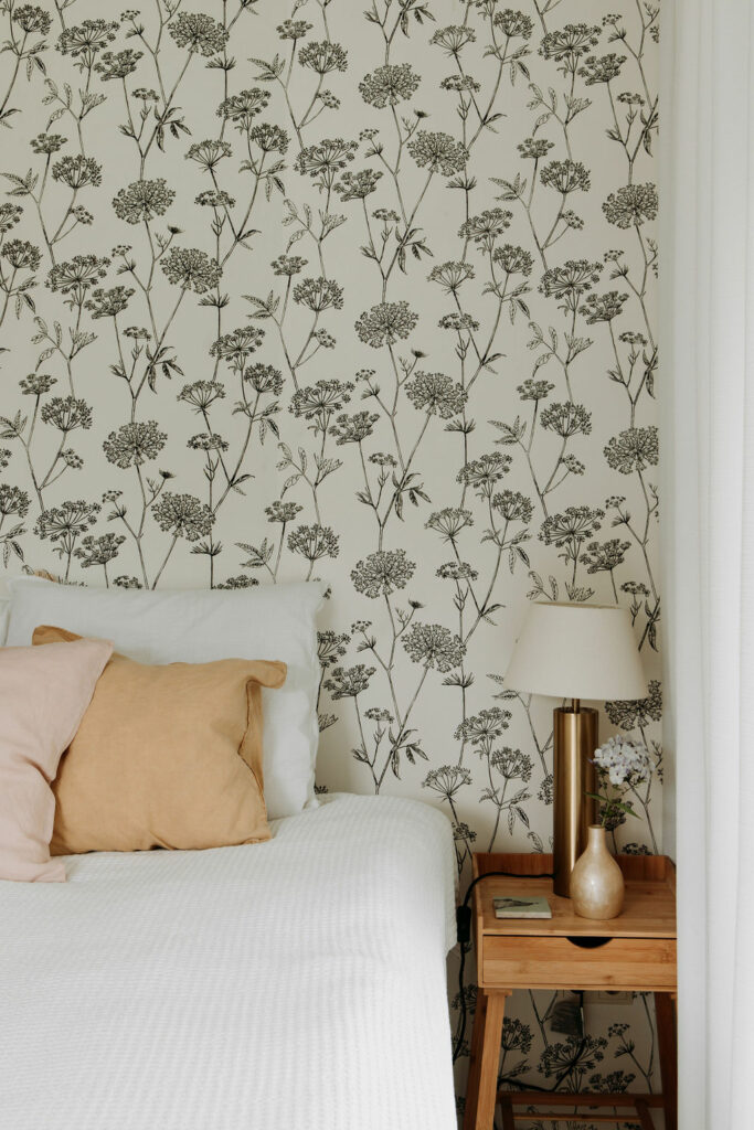 Twee persoonsbed met wit linnengoed met gekleurde sierkussens in de suite van B&B Erve Hasselo in Vorden. Op het behang staan schermbloemen. Op het nachtkastje staat een lamp en een vaasje met bloemen.
