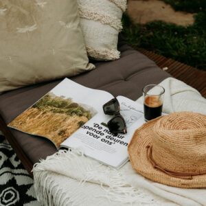 Sfeerimpressie van ligbed met kussens magazine, zonnebril koffie en hoed uit de fotogalerij mini camping Vorden.
